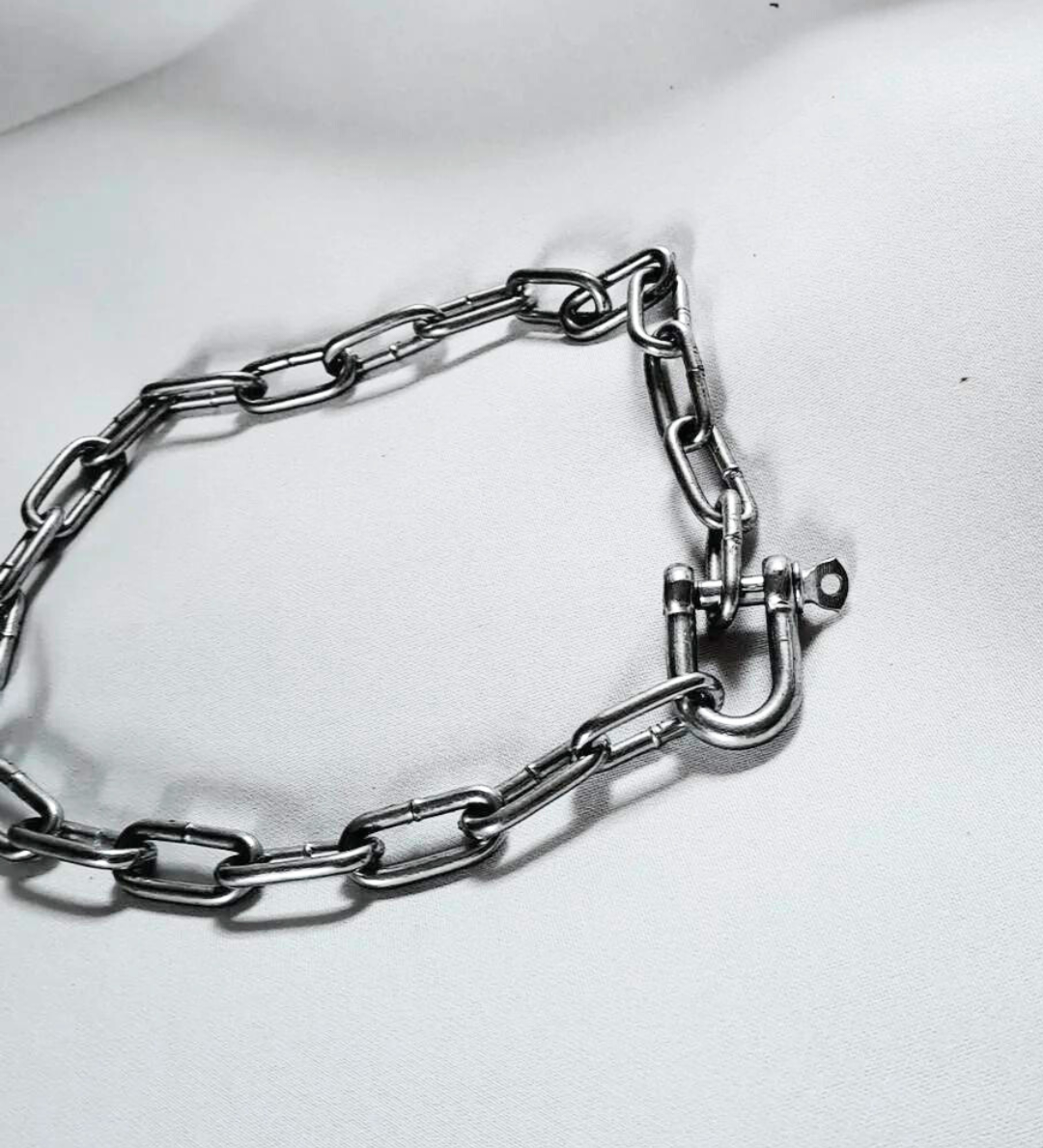 An angled shot of a silver stainless steel chain choker laid out on a white background.