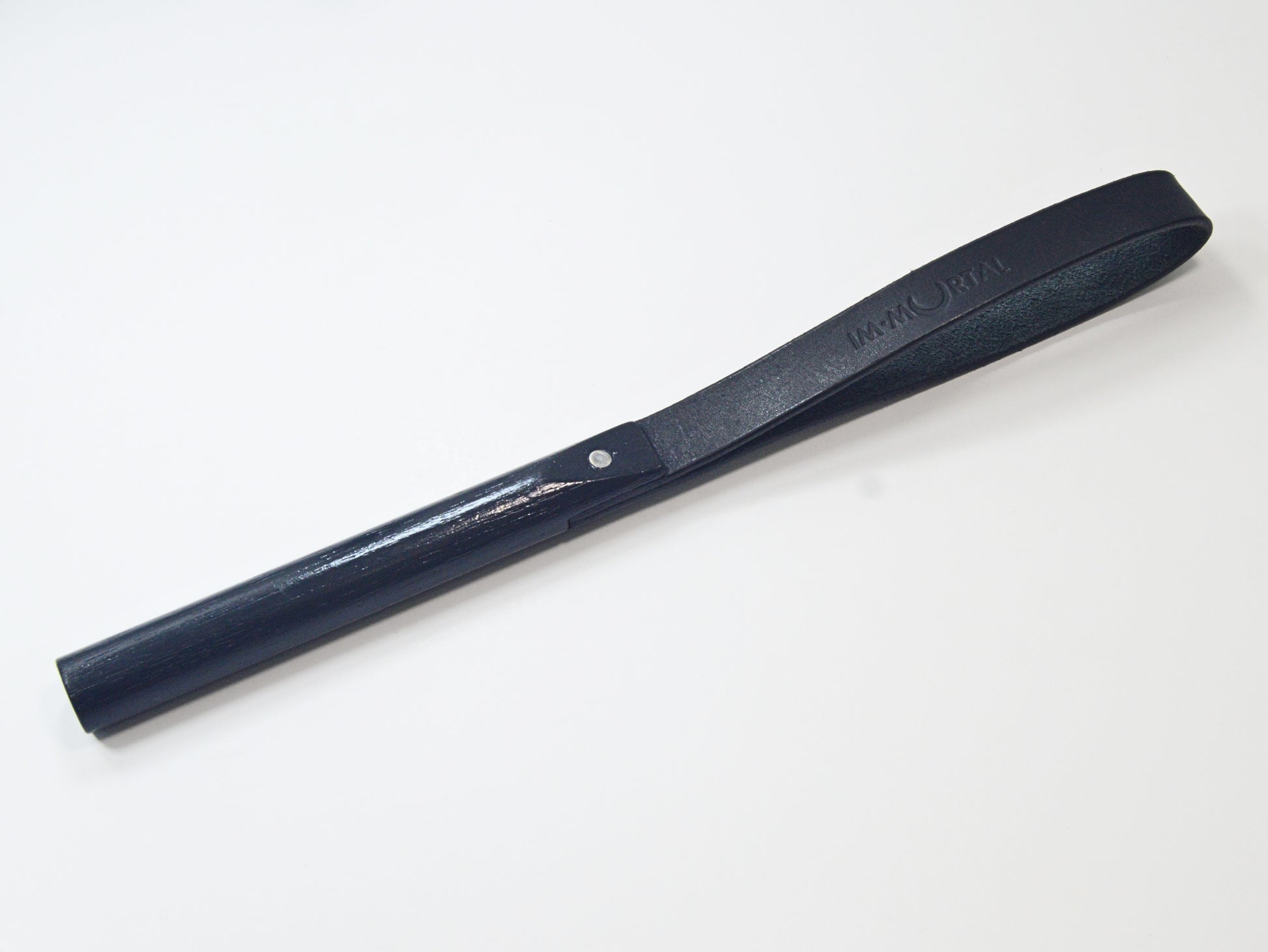 A black leather slapstick embossed with the word "IMMORTAL" with a wooden handle, showcased against a white background. It's designed for impact play.