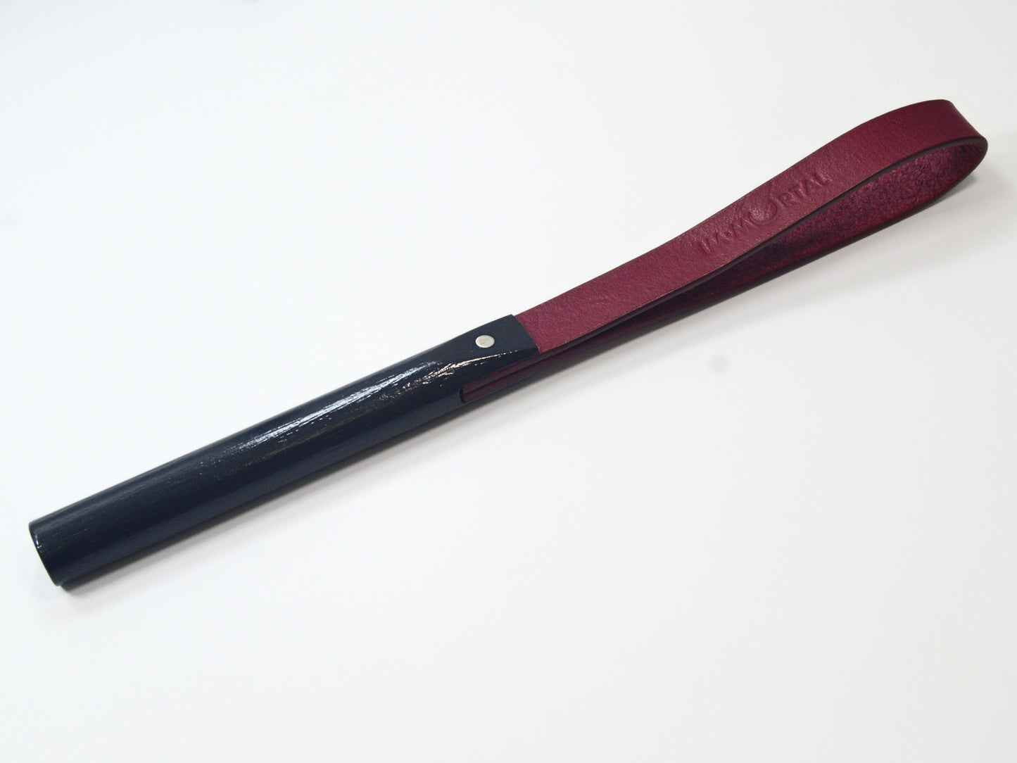 A burgundy leather slapstick embossed with the word "IMMORTAL" with a black wooden handle, showcased against a white background. It's designed for impact play.