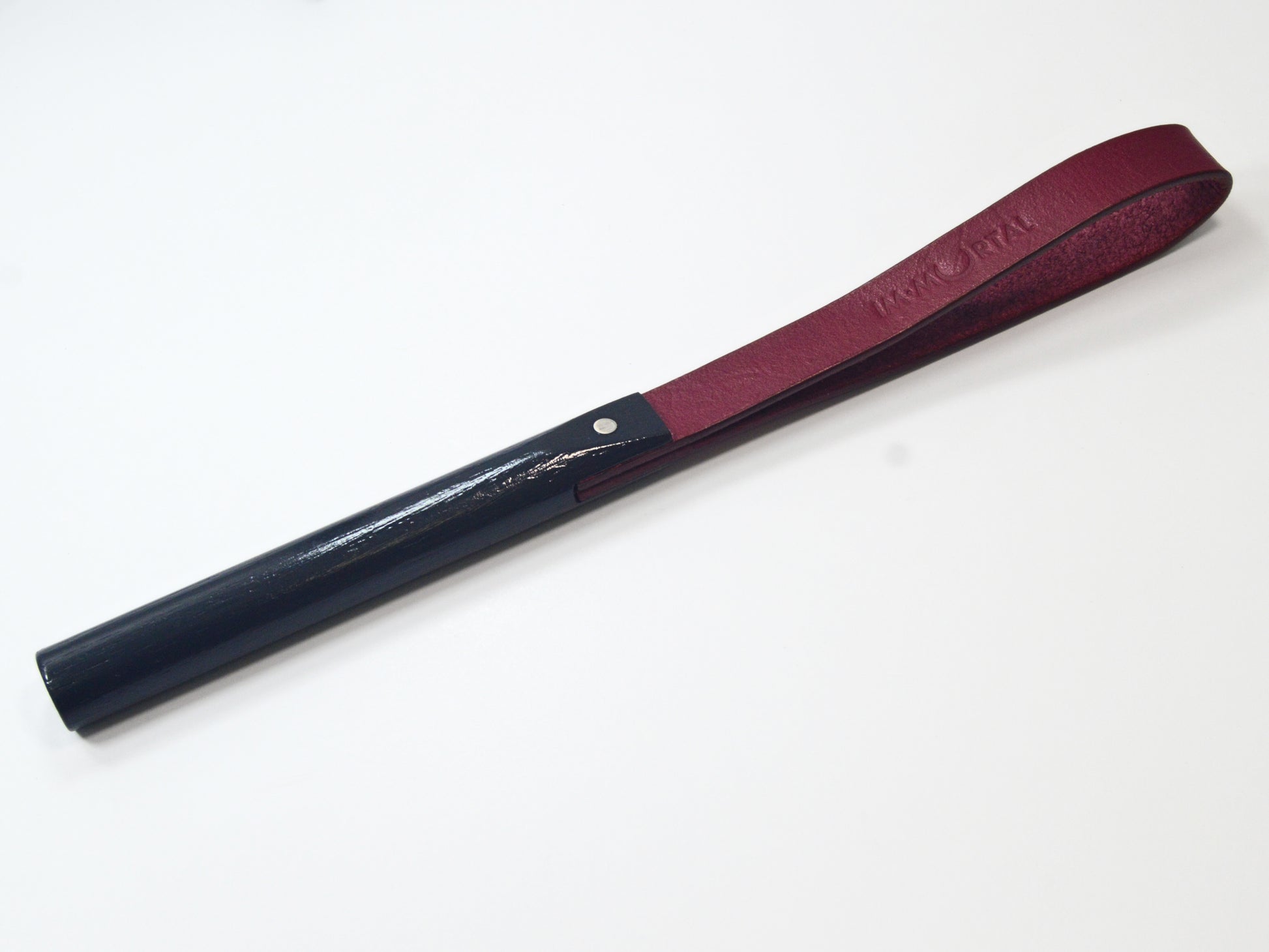 A burgundy leather slapstick embossed with the word "IMMORTAL" with a black wooden handle, showcased against a white background. It's designed for impact play.