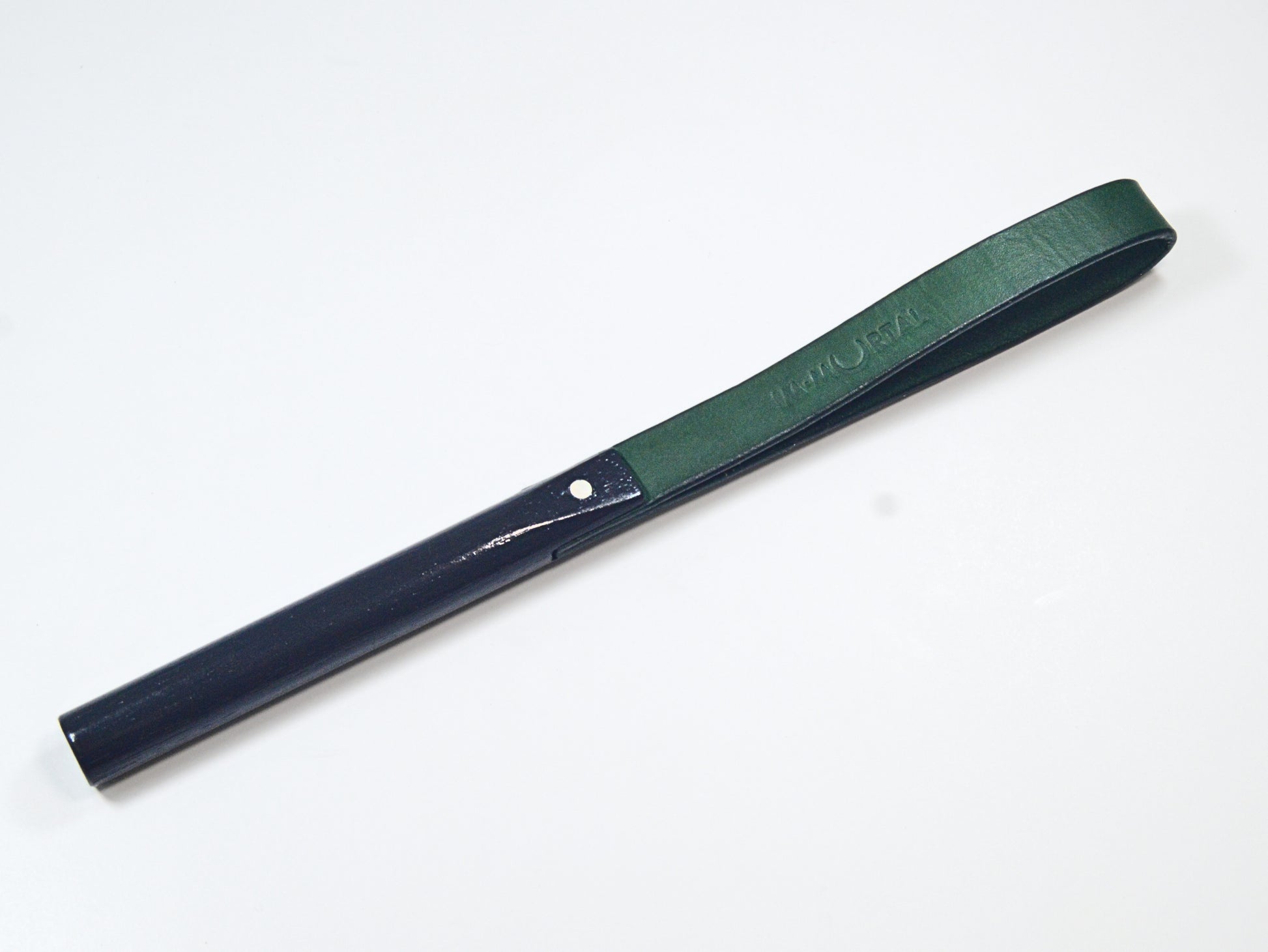 A green leather slapstick embossed with the word "IMMORTAL" with a black wooden handle, showcased against a white background. It's designed for impact play.