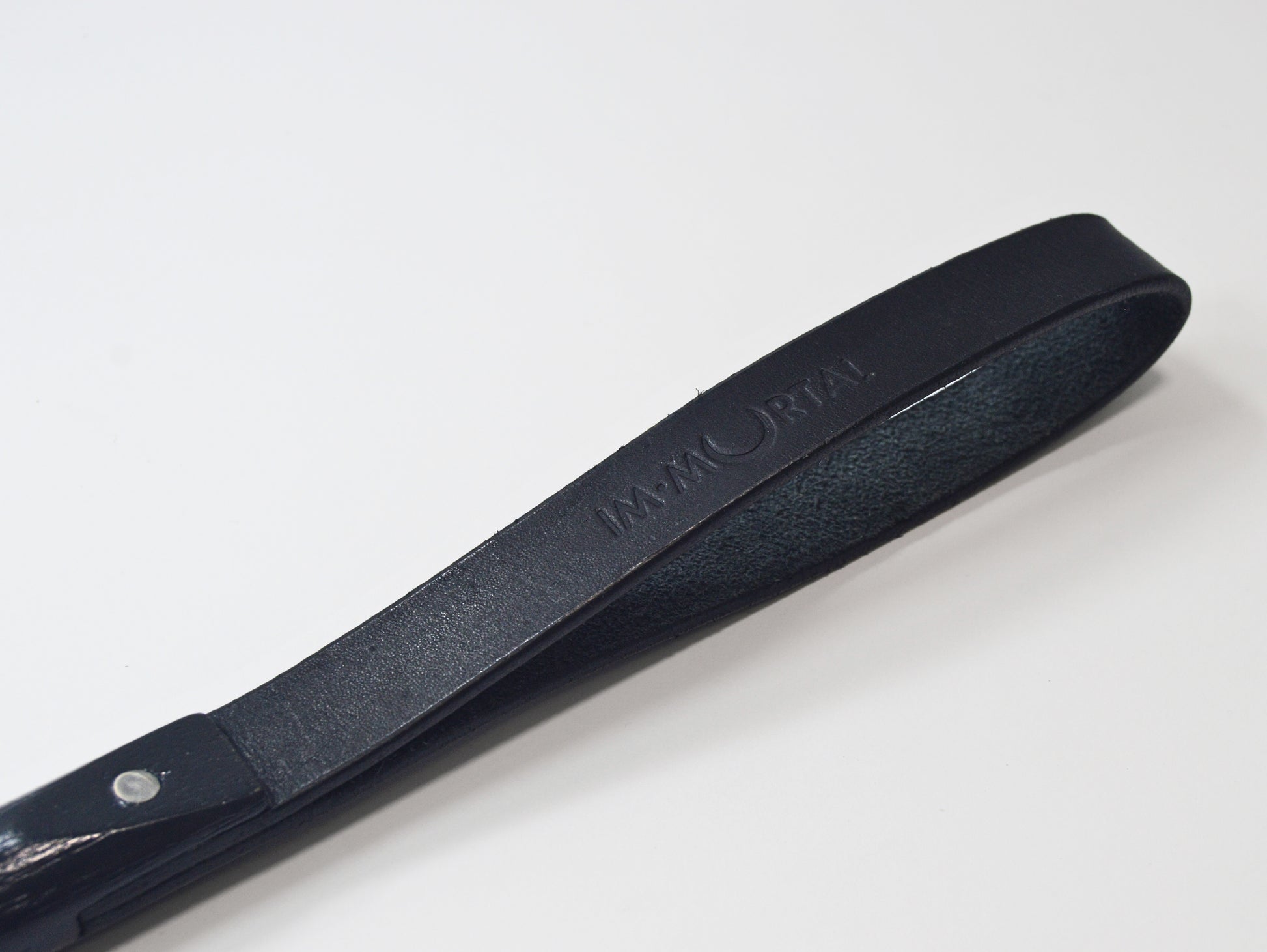 A close-up shot of the black leather slapstick strap embossed with the word "IMMORTAL" showcased against a white background.