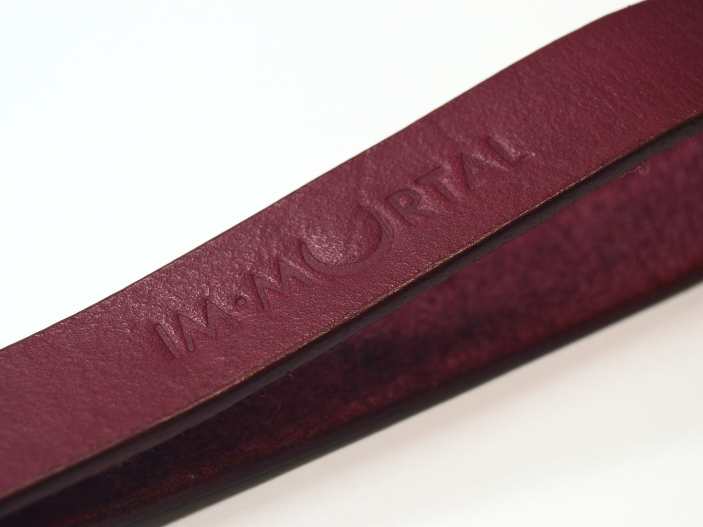 An extreme close-up shot of the embossed word "IMMORTAL" on the burgundy leather slapstick strap showcased against a white background.