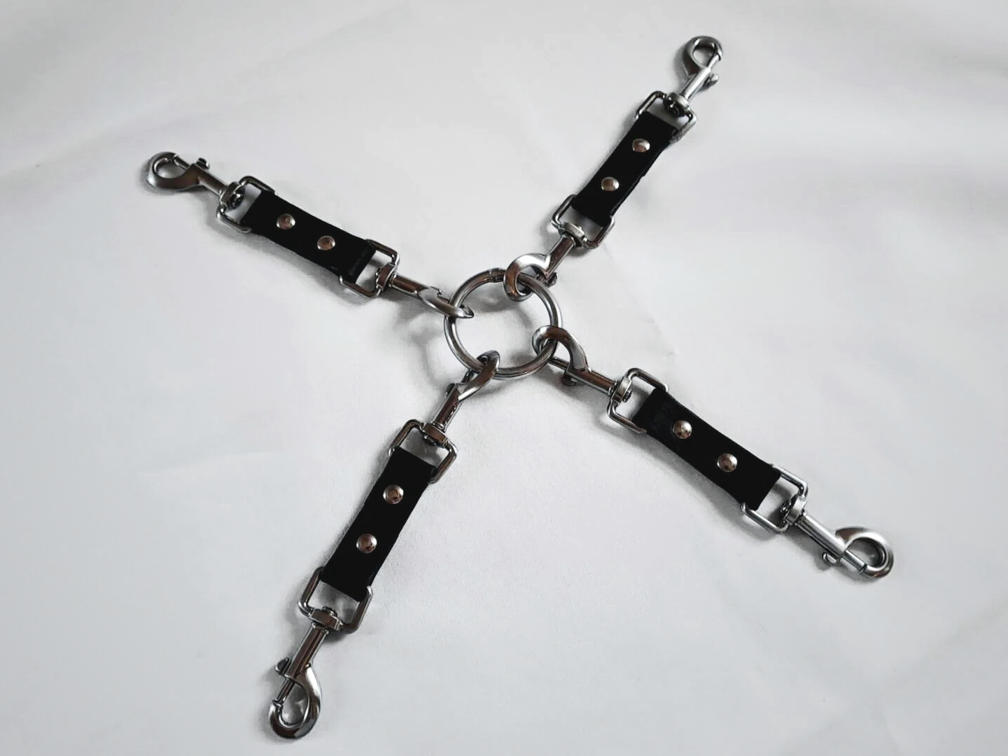 Four black leather straps with metal clasps are connected by a central metal ring (multi-functional leather hog-tie), displayed on against a white background.