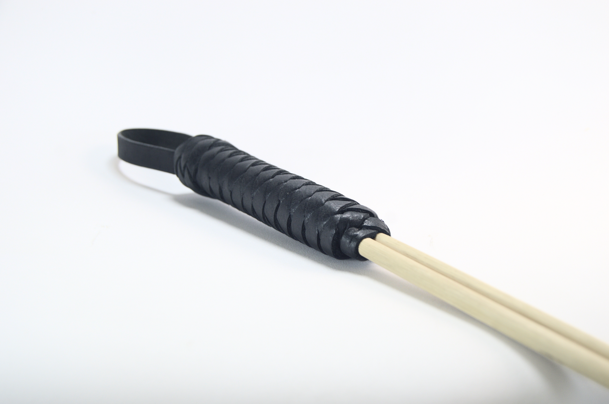 A close-up shot of the design of leather-weave wrapping on the end of a cane whip with a loop handle against a white background.