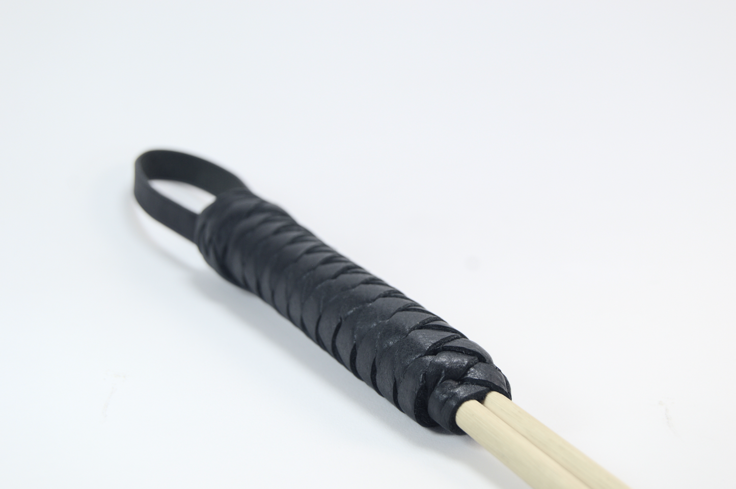 A close-up shot of the design of leather wrapped handle of a cane whip with a loop on the end against a white background.